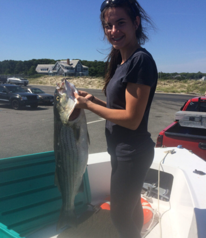 Girl on boat on trailer holding up striped bass