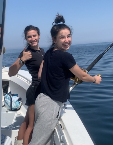 two happy teenage girls on the boat, thumbs up, pole out and line in the water