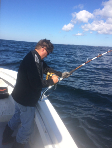 Man with large rod and reel reeling in a fish, ocean and blue sky in background