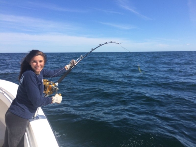 Girl on fishing charter boat, with fish on the line, reeling it in, smiling at camera