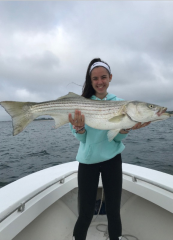 Young girl on boat, dark sky in background, holding four foot long striped bass