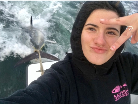 Selfie of girl and bluefin tuna tied behind boat, on the way home