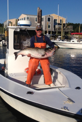 Captain Chris Hayes on the Ali J holding striped bass, dock in background