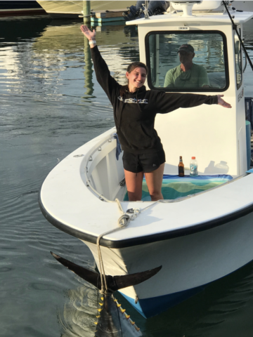 Girl on charter boat celebrating her catch of a bluefin tuna, tied to the bow of the boat by the tail